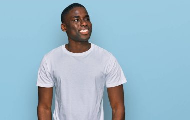 Gündelik beyaz tişört giyen Afro-Amerikan genç adam yüzünde gülümseme, doğal bir ifade ile yan yana bakıyor. Kendinden emin gülen. 