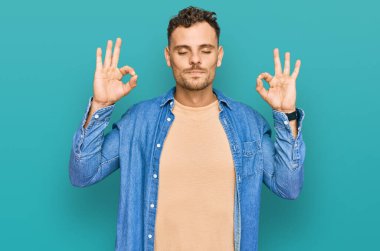 Günlük kıyafetler giyen genç İspanyol adam rahatla ve gözleri kapalı gülümse parmaklarıyla meditasyon hareketi yapıyor. yoga konsepti. 