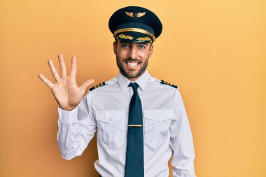 Yakışıklı İspanyol pilot üniforması giyen beş numarayı gösterip işaret eden kendinden emin ve mutlu gülümseyen adam.. 