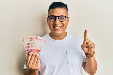 Elinde 10 Kolombiya pezosu olan genç bir Latin adam bir fikir veya soruyla gülümsüyor ve mutlu bir yüzle işaret ediyor. 