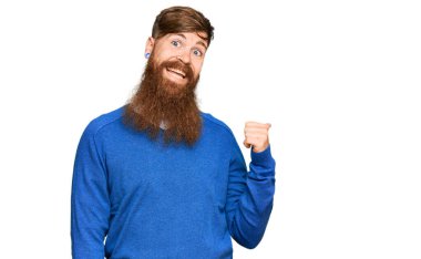 Genç İrlandalı kızıl saçlı, günlük kıyafetler giymiş mutlu yüzüyle gülümseyen ve başparmağıyla yan tarafı gösteren adam.. 