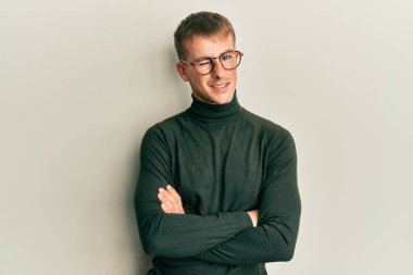 Kollarını kavuşturmuş gözlüklü genç beyaz adam kameraya seksi bir ifadeyle bakıyor, neşeli ve mutlu bir yüzle.. 