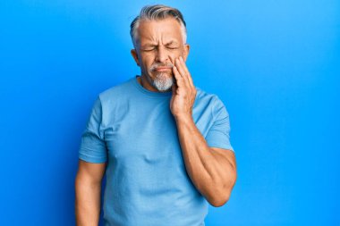 Orta yaşlı, gri saçlı, günlük kıyafetler giyen, diş ağrısı ya da diş hastalığından dolayı ağızlarına acı dolu bir ifadeyle dokunan bir adam. dişçi 