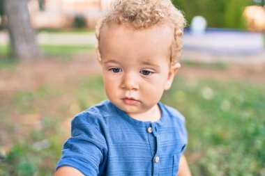 Sevimli ve mutlu küçük çocuk güneşli bir günde parkta eğleniyor. Güzel sarı saçlı erkek çocuk dışarıda oynuyor.