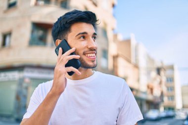 Genç Latin adam gülümsüyor ve şehirde akıllı telefondan konuşuyor..