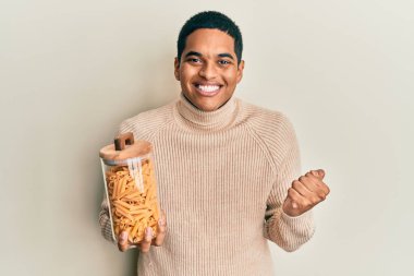 Genç, yakışıklı İspanyol adam elinde makarna kavanozuyla gururla bağırıyor zaferi ve başarıyı kutluyor. 