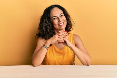 Masada el ele oturan, rahat ve neşeli gülümseyen orta yaşlı güzel bir kadın. Başarı ve iyimserlik 