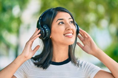 Genç İspanyol kadın gülümseyerek şehirde kulaklık takarak müzik dinliyor..