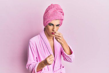 Kadın makyajı yapan genç adam kafasında duş havlusu ve bornozla yumruk savunma hareketleriyle kavga etmeye hazır kızgın ve üzgün bir yüz, sorundan korkuyor. 