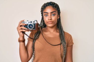 Saçları örgü örmüş, klasik fotoğraf makinesi takan, aklı başında, kendine güvenen genç Afrikalı Amerikalı bir kadın. 