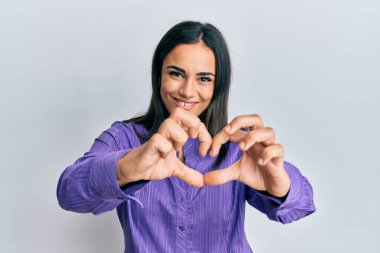 Genç esmer kadın, gündelik giysiler giyip, aşıkken gülümsüyor, elleriyle kalp sembolü yapıyor. romantik kavram. 