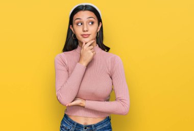 Elleri çenesinde gündelik giysiler içinde soru soran genç İspanyol kız, düşünceli ifade. Düşünceli bir yüzle gülümsüyor. şüphe kavramı. 