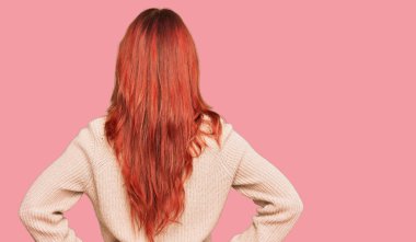 Kış süveteri giyen genç kızıl saçlı kadın kolları vücudunda geriye doğru bakıyor. 