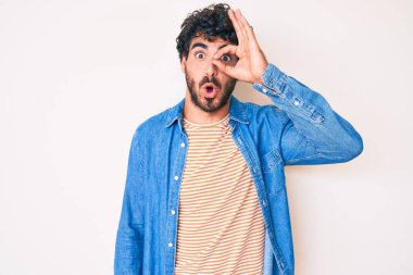 Kıvırcık saçlı ve ayı gibi sıradan bir kot ceket giyen yakışıklı genç adam şaşırmış yüz ifadesiyle şaşırmış, parmaklarından bakan bir hareket yapıyor. İnançsız ifade. 