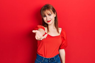 Kırmızı tişörtlü, neşeli gülümseyen, yardım eli uzatan ve kabul gören kızıl saçlı genç bir kadın.. 