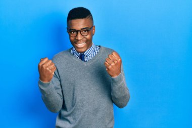 İş stili ve gözlük takan genç Afrikalı Amerikalı adam gururla bağırıyor, zaferi kutluyor ve başarıyı kollarını kaldırarak kutluyor. 