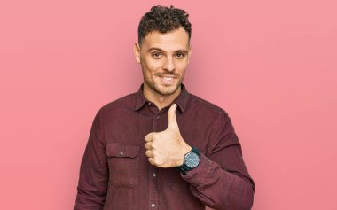 Gündelik kıyafetler giyen genç İspanyol adam elleriyle mutlu bir jest yapıyor. Kameraya bakıp başarıyı gösteren ifade. 