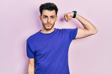 Gündelik tişört giyen genç İspanyol adam güçlü kol kası gösteren, kendinden emin ve gururlu biri. 