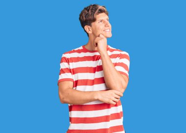 Elleri çenesinde gündelik giysiler giymiş soru soran, düşünceli bir genç adam. Düşünceli bir yüzle gülümsüyor. şüphe kavramı. 