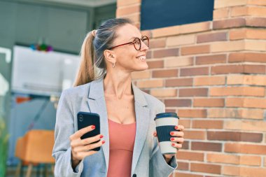 Genç sarışın iş kadını akıllı telefon kullanıyor ve şehirde kahve içiyor..