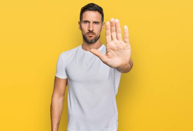 Gayri resmi beyaz tişört giyen sakallı yakışıklı adam avucunun içi gibi şarkı söylemeyi kesiyor. Yüzünde olumsuz ve ciddi bir jest olan uyarı ifadesi. 