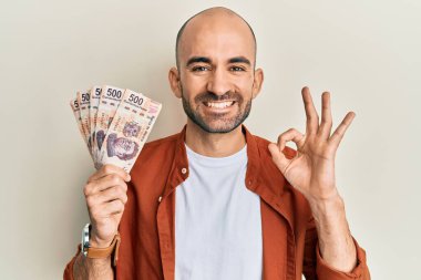 İspanyol asıllı genç adam 500 Meksika pezosu tutuyor. Parmaklarıyla imza atıyor, gülümsüyor. Mükemmel bir sembol. 