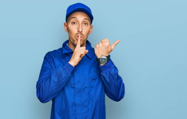 Sakallı, inşaatçı tulumu giymiş, kel bir adam sessiz olmak istiyor. Parmakları dudaklarında, elleri yandan işaret ediyor. sessizlik ve gizli konsept. 