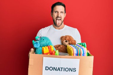 Genç ve yakışıklı bir adam bağış kutusunu tutuyor oyuncaklarla dilini çıkarıp komik bir ifadeyle mutlu oluyor.. 