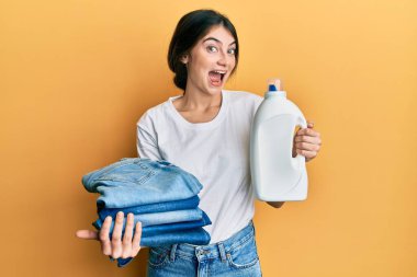 Çamaşır deterjanı şişesini ve katlanmış kotu tutan beyaz bir kadın çılgın ve başarıyı kutlarken gözleri açık heyecanla bağırıyor.. 