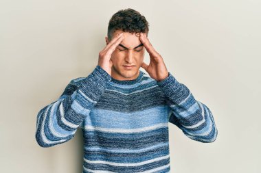 Latin kökenli genç adam, elleri kafasında, günlük bir kazak giyiyor, stres yüzünden baş ağrısı çekiyor. migren ağrısı. 