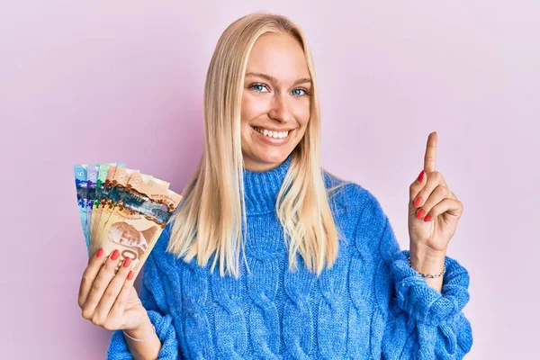 Młoda Blondynka Trzymająca Kanadyjskie Dolary Dużym Uśmiechem Twarzy Wskazująca Palcem — Zdjęcie stockowe