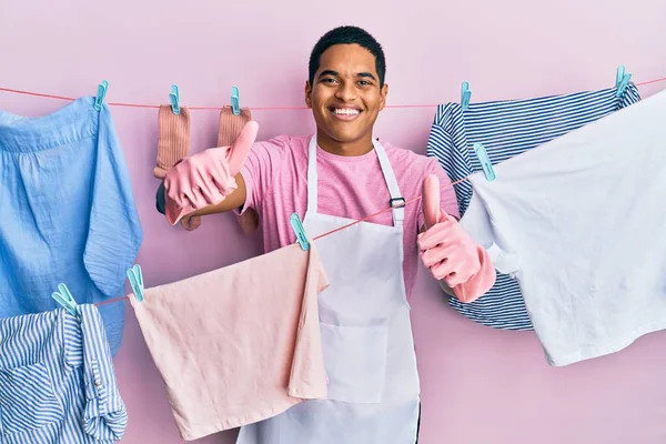 Joven Hombre Hispano Guapo Usando Delantal Más Limpio Sosteniendo Ropa —  Fotos de Stock