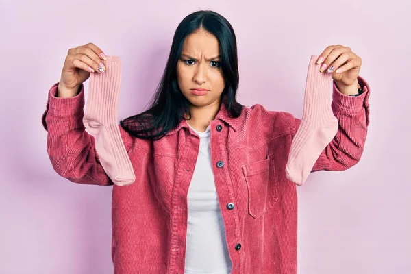 Beautiful hispanic woman with nose piercing holding socks skeptic and nervous, frowning upset because of problem. negative person.