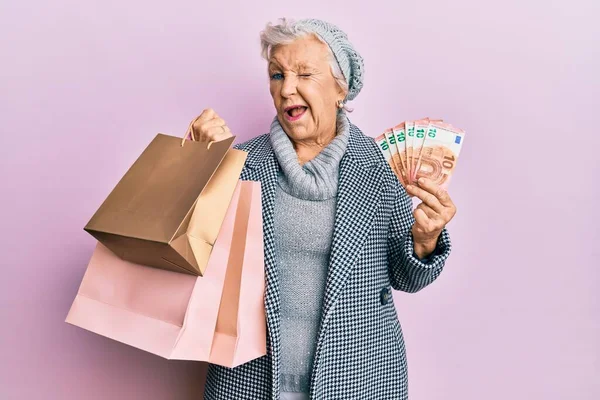 Senior Grey Haired Woman Holding Shopping Bags Euros Banknotes Winking — Stock Fotó