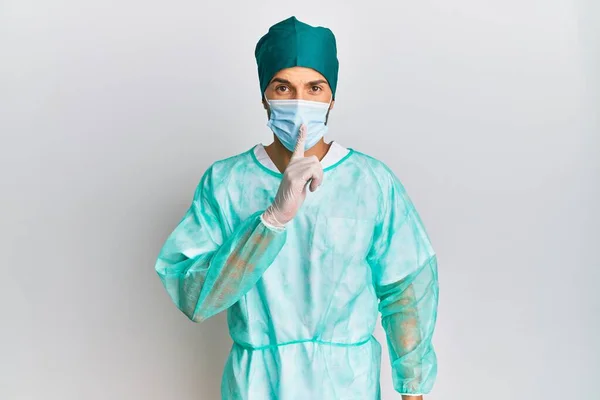 外科医の制服を着た若いハンサムな男と医療マスクは唇に指で静かにするように求めています 沈黙と秘密の概念 — ストック写真