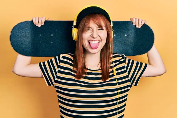 Κοκκινομάλλα Νεαρή Γυναίκα Κρατώντας Skate Φορώντας Ακουστικά Κολλήσει Γλώσσα Έξω — Φωτογραφία Αρχείου
