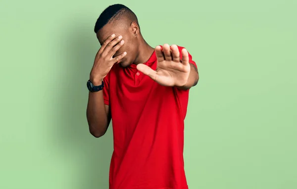 若いアフリカ系アメリカ人の男性は カジュアルな赤いTシャツを着て手で目を覆い 悲しいと恐怖の表情でジェスチャーを止めます 恥をかかせ否定的な概念 — ストック写真