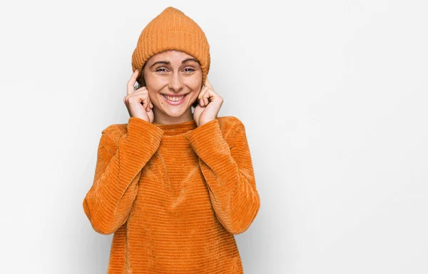 カジュアルな服を着た若いヒスパニック系の女性や 大きな音楽のノイズのためにいらいらする表情で指で耳を覆うウールキャップ 聴覚障害の概念 — ストック写真