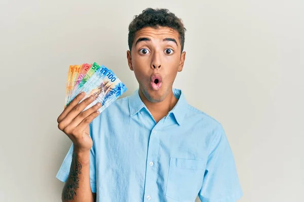 Joven Hombre Afroamericano Guapo Sosteniendo Billetes Franco Suizos Asustado Sorprendido —  Fotos de Stock