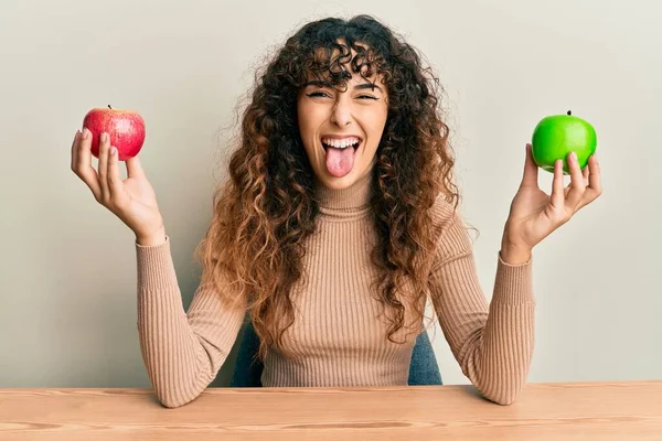 Joven Chica Hispana Sosteniendo Manzanas Sentadas Mesa Sacando Lengua Feliz — Foto de Stock