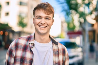 Genç beyaz adam gülümseyerek şehirde mutlu mesut duruyor..