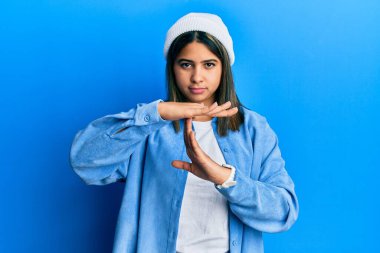 Tatlı yün şapka takan genç Latin bir kadın. El kol hareketi yapıyor, hayal kırıklığına uğramış ve ciddi bir yüz ifadesi takınıyor. 