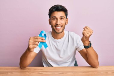 Mavi kurdele tutan yakışıklı genç adam gururla haykırıyor, zaferi kutluyor ve başarıyı kollarını kaldırarak kutluyor. 