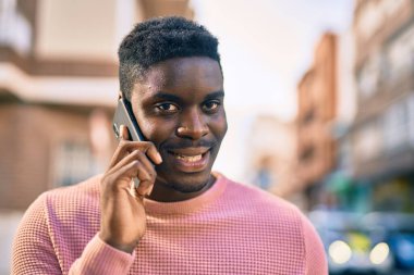 Genç Afrikalı Amerikalı gülümseyen mutlu bir adam şehirdeki akıllı telefondan konuşuyor..