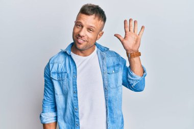 Yakışıklı, sıradan kot ceket giyen kaslı adam beş numarayı gösterip işaret ederken kendinden emin ve mutlu gülümsüyor.. 