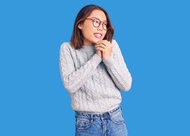 Genç, güzel Çinli kız rahat kıyafetler giyiyor. Gergin ve heyecanlı bir şekilde gülüyor. Elleri çenesine bakıyor. 