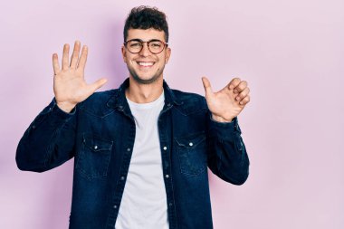 Gündelik kıyafetler giyen ve gözlük takan İspanyol genç adam altı numarayı gösterip işaret ederken kendinden emin ve mutlu gülümsüyor.. 