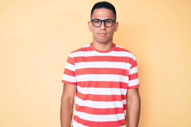 Yüzünde ciddi bir ifade olan gündelik kıyafetler ve gözlük takan genç, yakışıklı Latin bir adam. Basit ve doğal bir şekilde kameraya bakıyorsun.. 