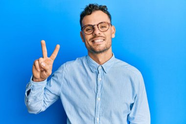 Gündelik kıyafetler ve gözlük takan genç İspanyol adam kameraya bakıp zafer işareti yapıyor. İki numara.. 