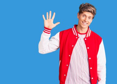 Beyzbol üniforması giyen yakışıklı genç adam beş numarayı gösterip işaret ederken kendinden emin ve mutlu bir şekilde gülümsüyor.. 